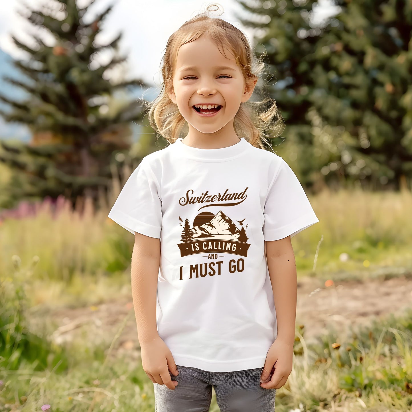 Smiling toddler wearing “Switzerland Is Calling” t-shirt in white with mountain design outdoors