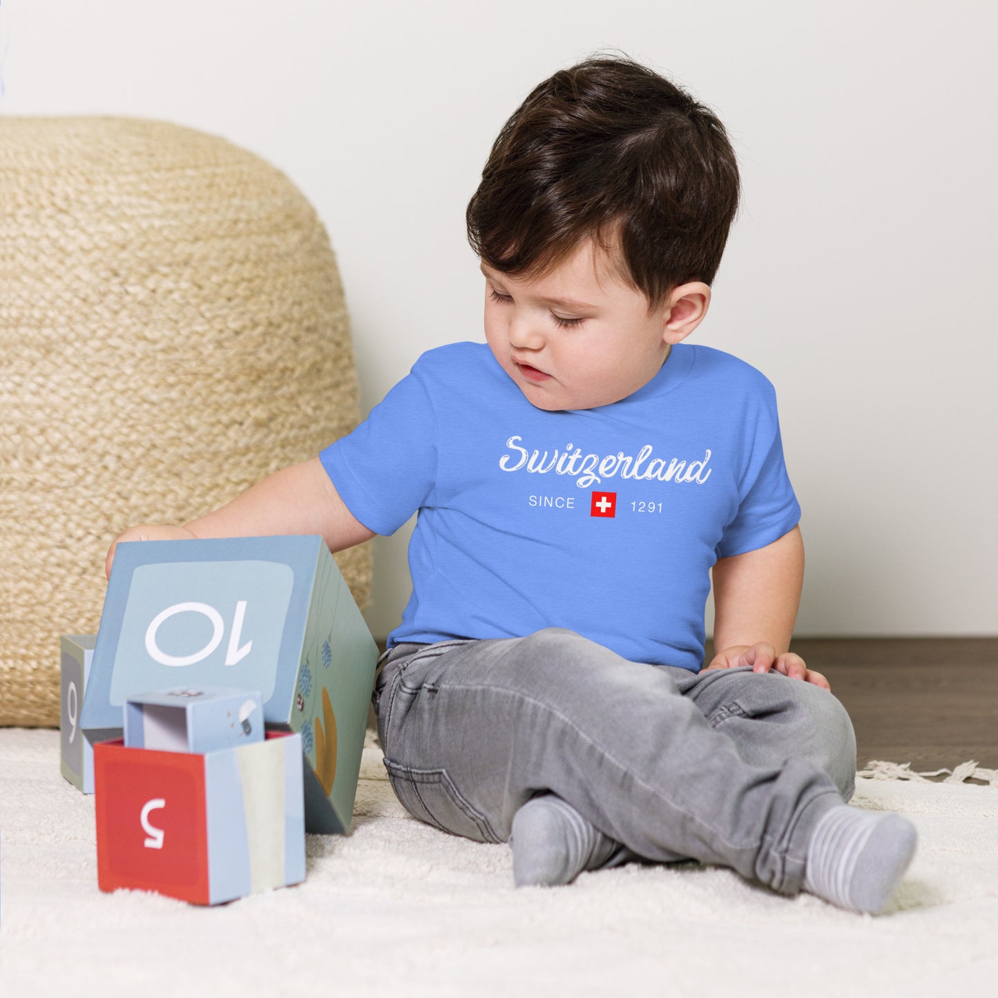 Toddler sitting down in Switzerland-themed t-shirt with national pride design.