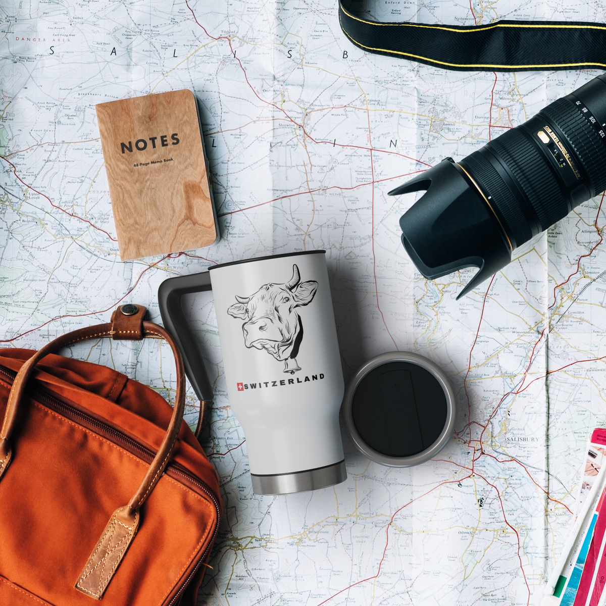 Swiss cow Switzerland travel mug displayed with camping and travel accessories