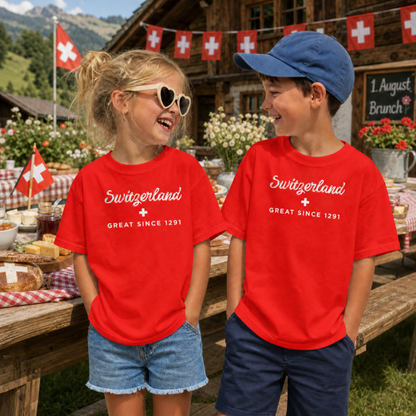 Two children standing outdoors in front of a rustic Swiss Farm August 1 brunch, wearing matching bright red T-shirts with white 'Switzerland Great Since 1291' text and a Switzerland flag cross. 