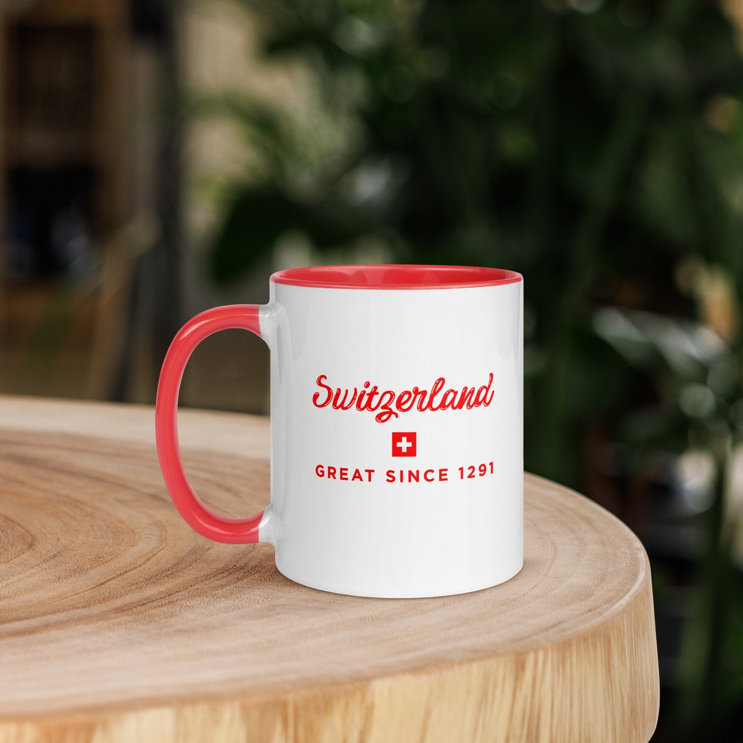 A white ceramic mug with a red interior, red handle, and red printed text reading 'Switzerland' and 'GREAT SINCE 1291' with a small Swiss flag. 