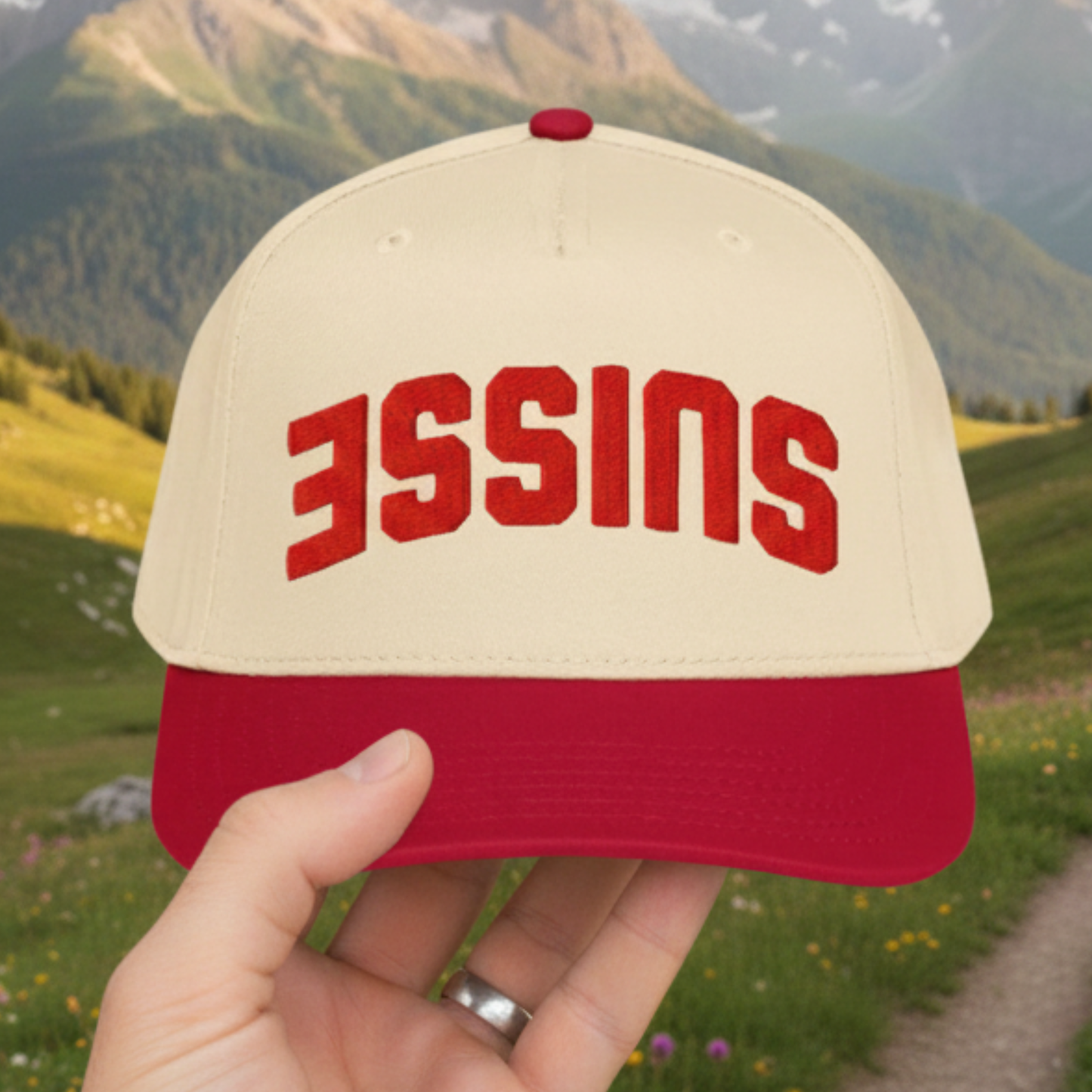 Suisse upside-down trucker hat with 3D puff embroidery held in front of Swiss Alps landscape