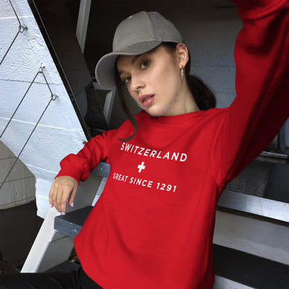 A woman wearing a bright red long-sleeve sweatshirt with white text reading 'SWITZERLAND' and 'GREAT SINCE 1291' on the chest