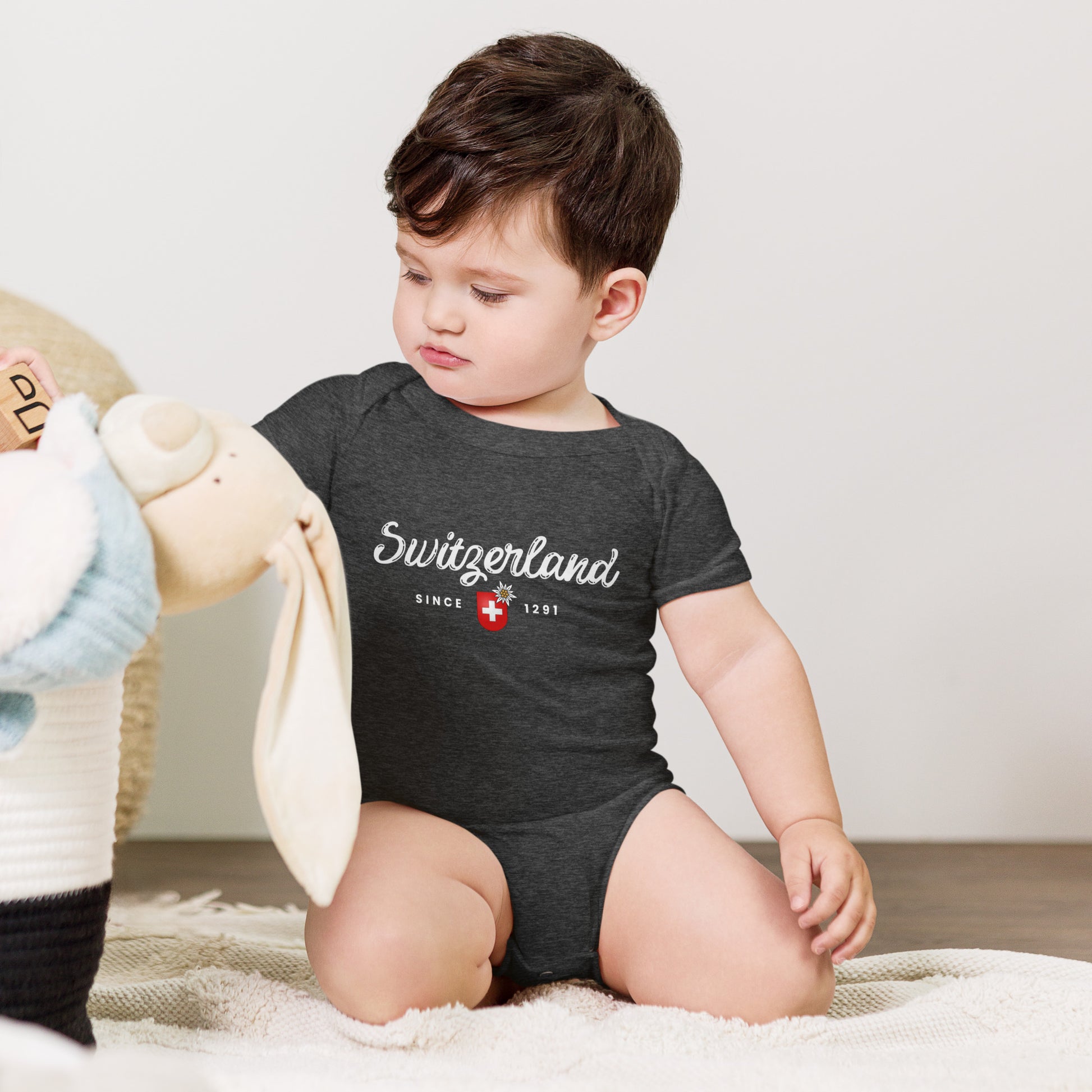Baby wearing dark gray Switzerland Since 1291 onesie with red Swiss flag