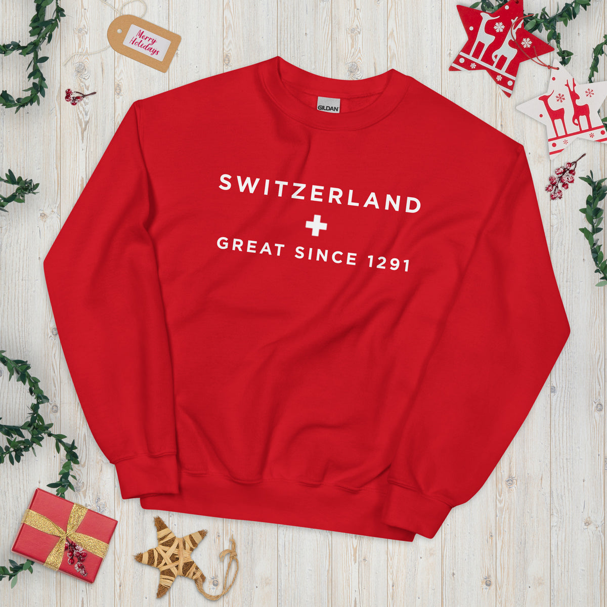 A red crewneck sweatshirt with white text reading 'SWITZERLAND + GREAT SINCE 1291' with Christmas decorations around it.